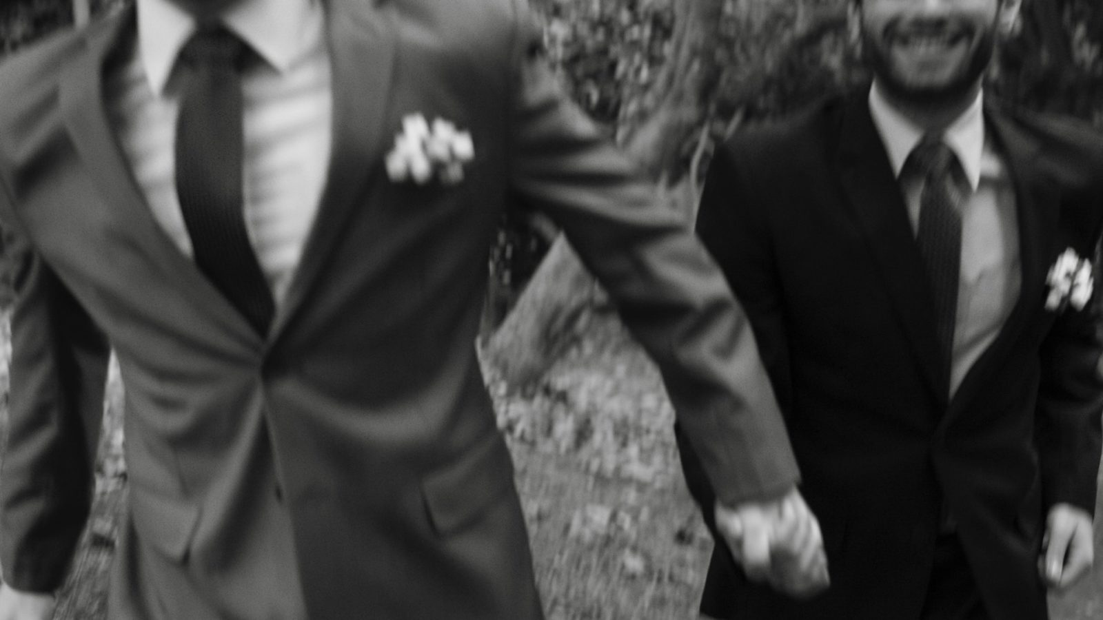 man in black suit holding hands with another man in grey suit