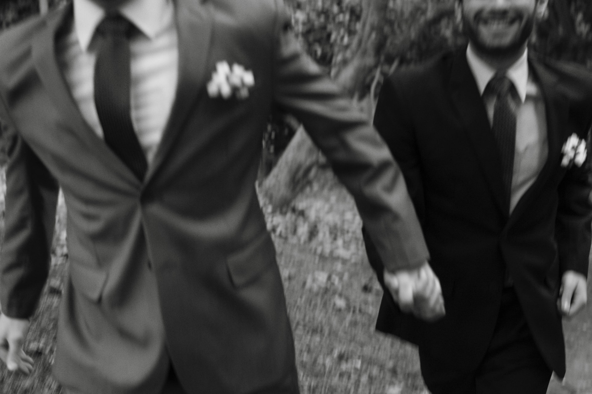 man in black suit holding hands with another man in grey suit